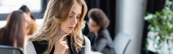 pensive businesswoman touching chin near multiethnic colleagues on blurred background, banner - Foto, Bild