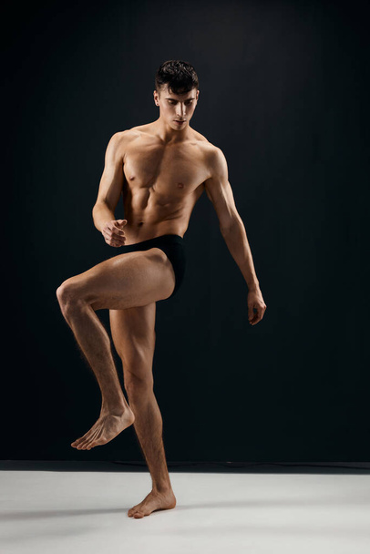 fisiculturista masculino com um corpo musculado em calcinhas escuras posando - Foto, Imagem