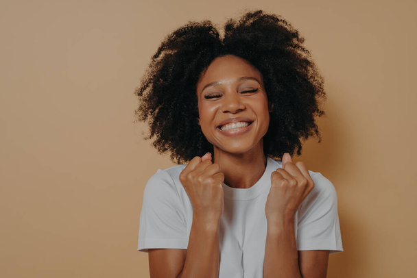 Щаслива щаслива темношкіра молода жінка піднімає прикуті кулаки і посміхається
 - Фото, зображення