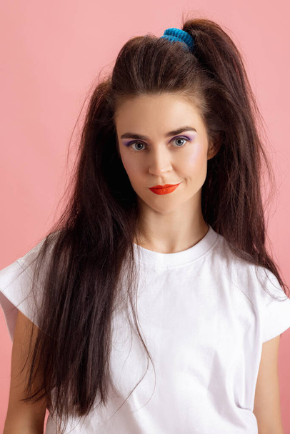 Close-up adorable pretty young girl with bright makeup and hairdo in retro 90s fashion style isolated over pink studio background. Concept of eras comparison, beauty, fashion and youth. - Foto, imagen
