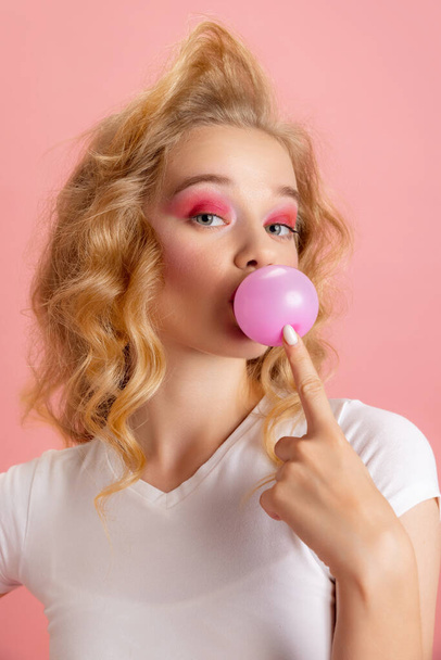 Close-up adorable pretty young girl with bright makeup and hairdo in retro 90s fashion style isolated over pink studio background. Concept of eras comparison, beauty, fashion and youth. - Foto, Imagem