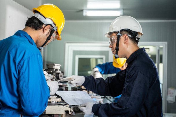 Asyalı mekanik işçiler değirmen makinesinde çalışıyor. Güvenlik önlemi için makineyi çalıştırırken koruyucu gözlük ve kask takan teknisyenler. Lider, ekip üyesine bir iş yapmasını tavsiye ediyor - Fotoğraf, Görsel