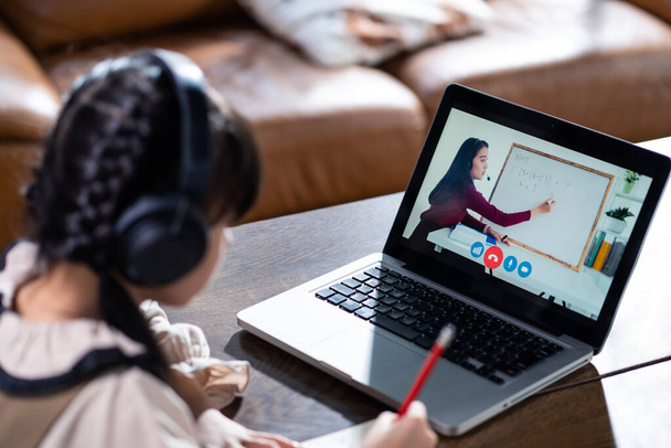 Homeschool ázsiai fiatal lány tanul online tanítani tanár digitális távoli internet találkozó miatt coronavirus pandemic. Aranyos gyerek tanulmány otthon, nézi a számítógép laptop videó. - Fotó, kép