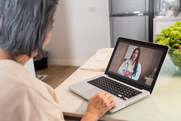 Asian senior woman video call with doctor in living room at home. Elder patient consulting with general practitioner application computer laptop. Doctor and Consultant online and telemedicine concept. - Photo, Image