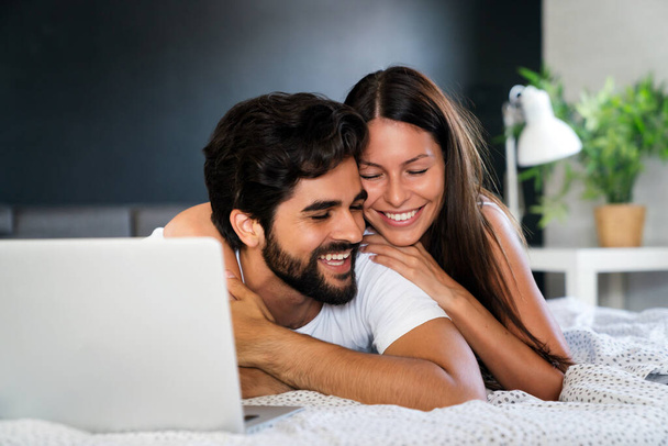 Happy couple with laptop in bed reading news and smiling - Fotografie, Obrázek