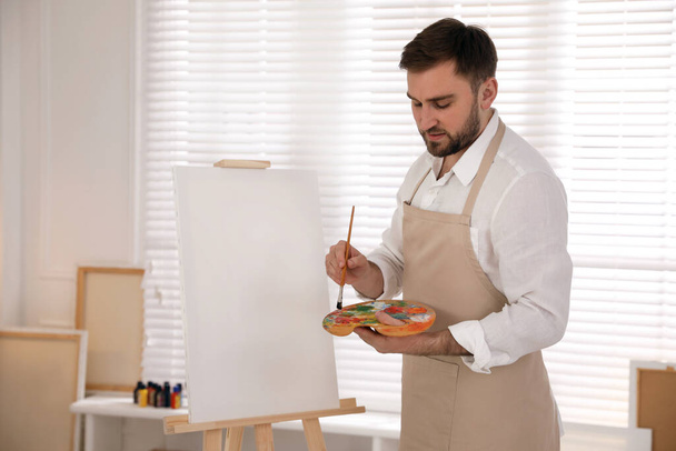 Young man painting on easel with brush in artist studio - Foto, Imagen