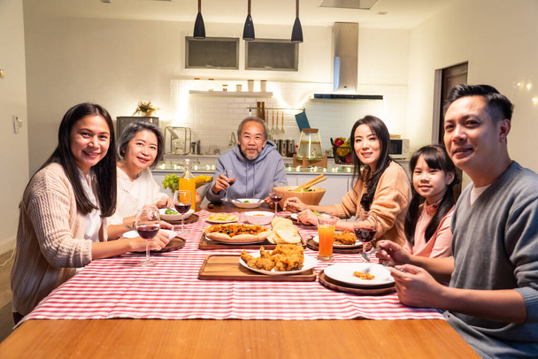 Retrato de la gran familia feliz asiática cenando juntos en casa. Abuelo anciano mayor pasar tiempo con un joven visitante familiar comer comida en la mesa y disfrutar de la fiesta y luego mirar a la cámara en casa - Foto, imagen