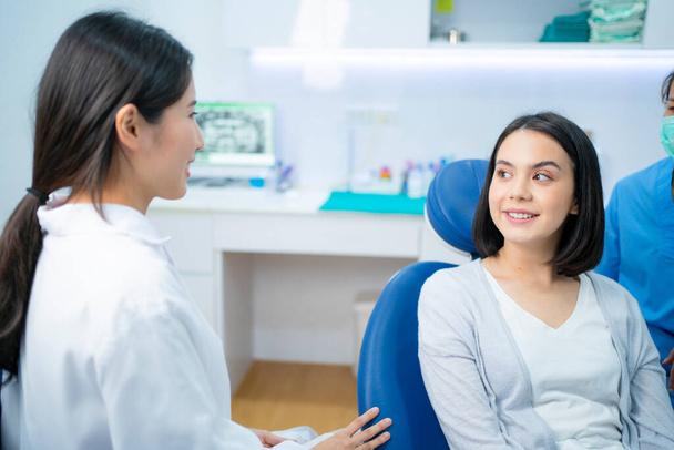 Кавказская красавица разговаривает и консультируется с азиаткой-стоматологом по поводу кариеса и заболевания десен в зубной клинике. Молодая женщина счастлива получить заботу от профессионального стоматолога - Фото, изображение
