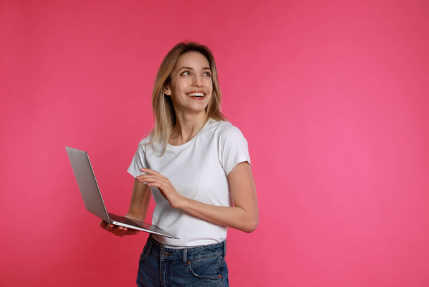 Young woman with modern laptop on pink background - 写真・画像