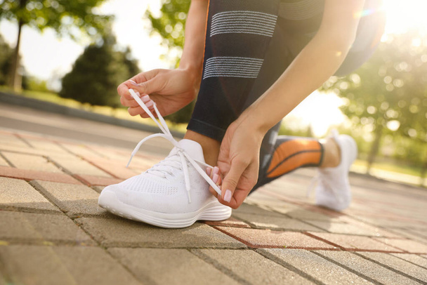 Woman tying laces of sneakers outdoors, closeup. Morning fitness - Foto, Imagen