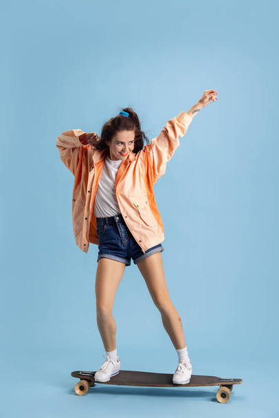 Beautiful adorable young girl in retro 90s fashion style, outfits on skateboard isolated over pink studio background. Concept of eras comparison, beauty, fashion and youth. - Foto, imagen