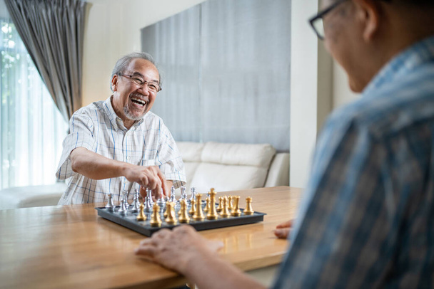 Azjatycki starszy mężczyzna spędza wolny czas, zostaje w domu po przejściu na emeryturę. Szczęśliwy uśmiechnięty Starzec cieszyć się aktywnością w domu gry w szachy z przyjacielem razem. Szpital Opieka zdrowotna i koncepcja medyczna - Zdjęcie, obraz