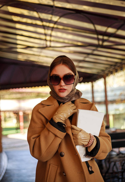 Fashionable young lady in a long beige coat at the restaurant site, autumn clothing style - Фото, изображение