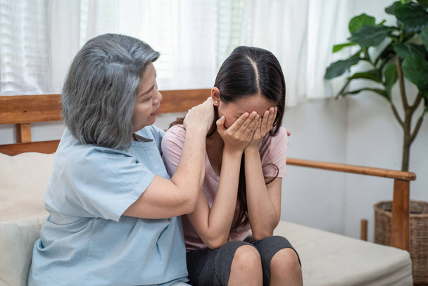 Asian loving elderly mother consoling and comforting upset depressed young girl daughter crying for problem. Caring Senior mom support and understanding empathy to stressed woman in tears at home. - Photo, Image