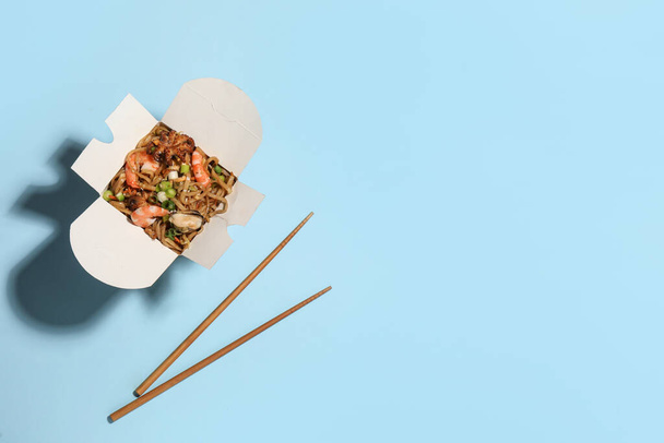 Noodle wok with chopsticks on light blue background, flat lay. Space for text - Фото, изображение