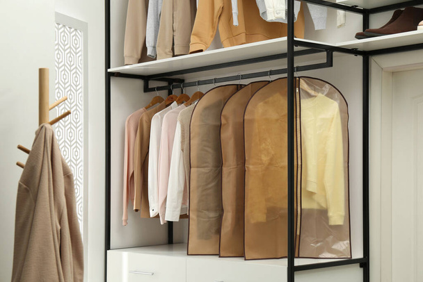 Garment bags with clothes on rack in dressing room - Foto, Imagen