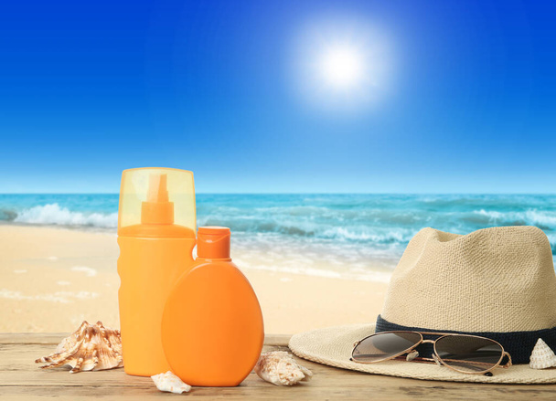 Bottles of skin sun protection products and beach accessories on wooden table against seascape. Space for design - Foto, Imagen