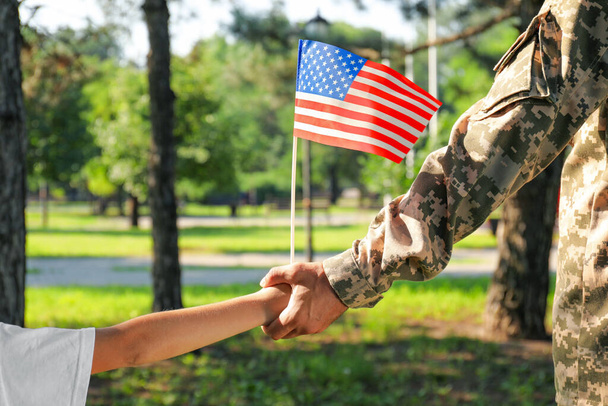 Soldier and his little son with American flag holding hands outdoors, closeup. Veterans Day in USA - 写真・画像