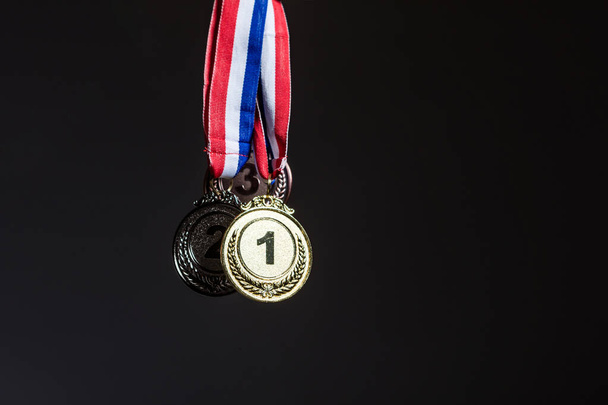 Vor dunklem Hintergrund hängen drei Gold-, Silber- und Bronzemedaillen. Sport und Siegeskonzept. - Foto, Bild