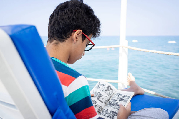Teenage boy sitting on pier chair and enjoying summer - Foto, imagen