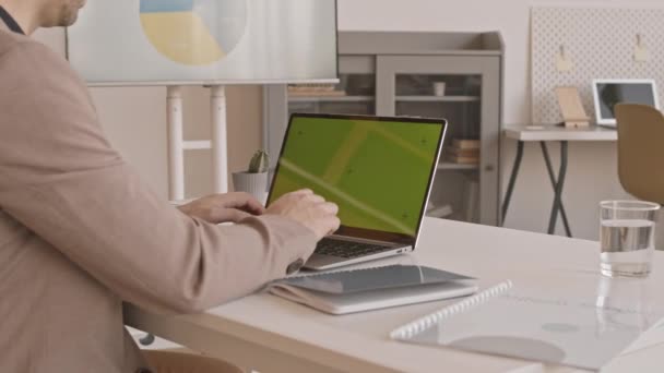 Arc shot du gestionnaire recadré en costume formel, assis sur le lieu de travail, tapant sur le clavier de l'ordinateur portable avec écran vert - Séquence, vidéo