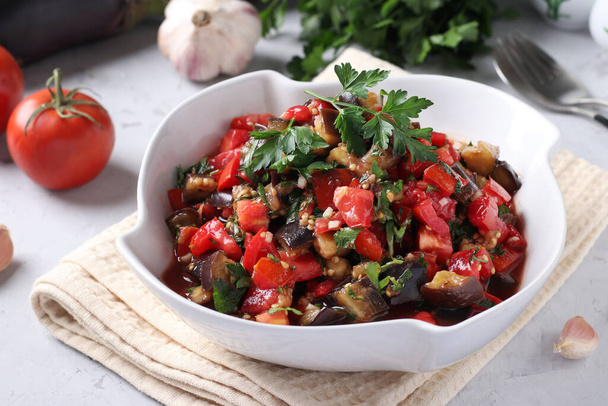 Salad with eggplants, tomatoes, garlic and parsley in a white bowl on a light gray background. Close-up - Foto, Bild