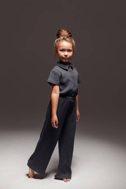 A cute little girl in a jumpsuit poses in isolation against a dark background in the studio. fashion photography. - Фото, изображение