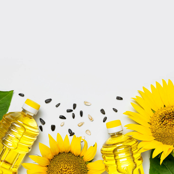 Plastové láhve se slunečnicovým olejem, čerstvé žluté slunečnice, slunečnicová semínka na šedém pozadí. Doba sklizně zemědělské produkce oleje. Zdravé oleje, jídlo. Flat lay top view copy space. - Fotografie, Obrázek