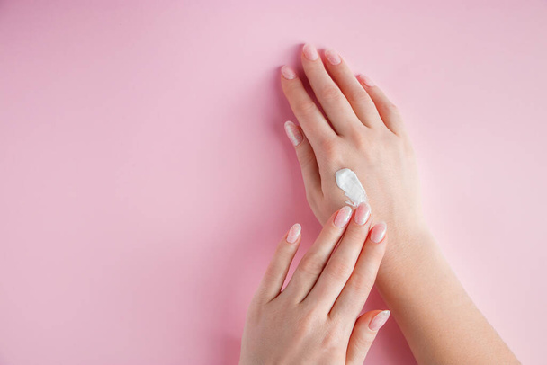 A young woman is applying cream to her hands. Spa and body care concept on pink background. Place for text. - 写真・画像