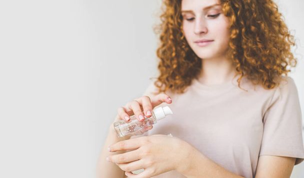 beautiful woman with red afro hairsty leapplying cosmetic cream treatment on her face. close-up hand with serum bottle, face blurred. - 写真・画像