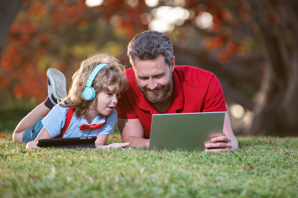pai e filho usam laptop para videochamada ou lição ouvir música em fones de ouvido no parque, educação. - Foto, Imagem