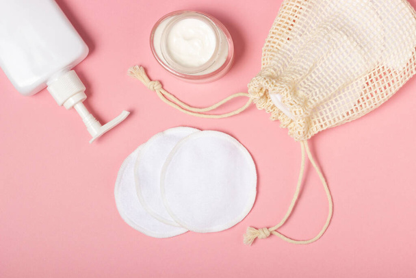 Cotton reusable make-up remover pads in a cloth bag and face wash and cleanser on a pink background. The concept of ecology and conscious consumption. Reusable cotton pads - Foto, imagen