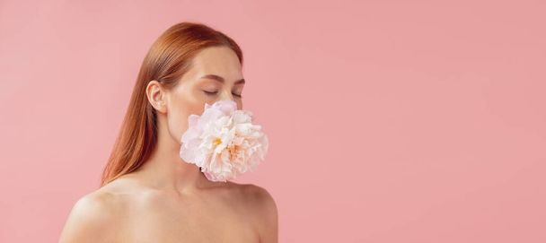 Natural beauty. Close-up portrait of beautiful redheaded woman with flower isolated over pink studio back ground. - Zdjęcie, obraz