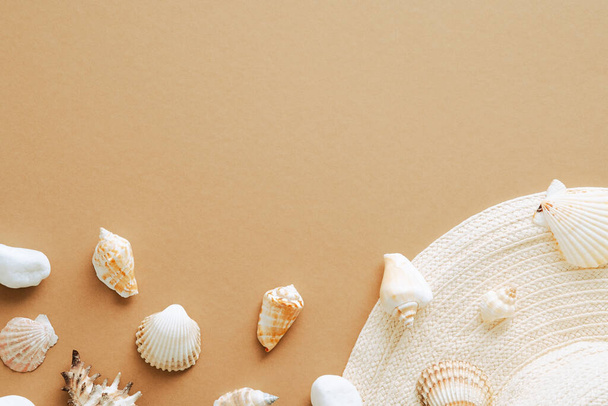 Summer flat lay composition with straw hat and seashells on sandy color background. Top view, overhead. - Foto, Imagen