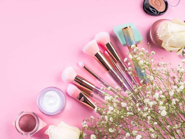 Trendy make-up borstels met producten op roze achtergrond met gypsophila bloemen - Foto, afbeelding