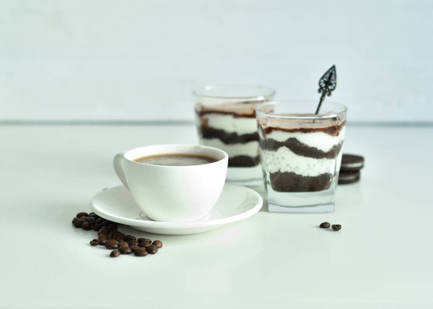 cup of black coffee and coffee beans, dessert in a glass. Cheesecake with chocolate and cottage cheese cream on white background. Good morning concept. Copy space. Selective focus. - Photo, Image