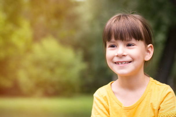 Happy little girl in a yellow t-shirt is looking away on a green background - Foto, imagen
