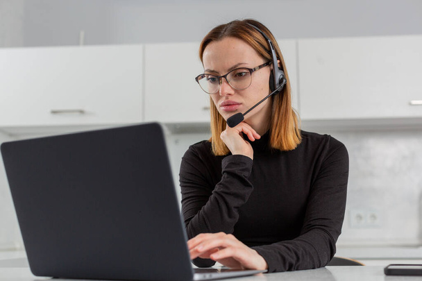 A female call center employee in a headset looks up at a laptop monitor  - Φωτογραφία, εικόνα