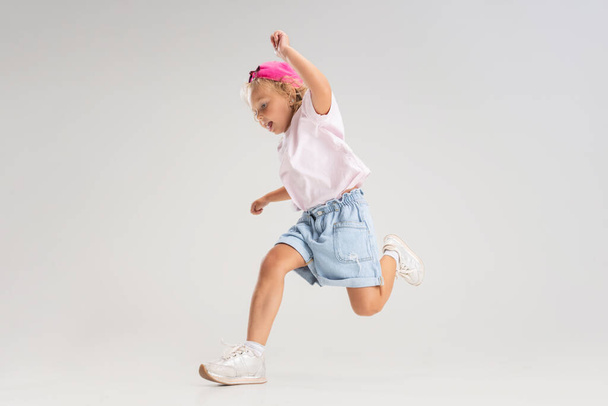 Studio image of little preschool Caucasian girl in casual clothes running, jumping isolated over white studio background. - 写真・画像