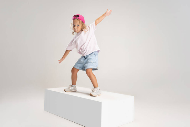Танцующий хип-хоп. Портрет маленькой белой дошкольницы в повседневной одежде на белом фоне студии. - Фото, изображение