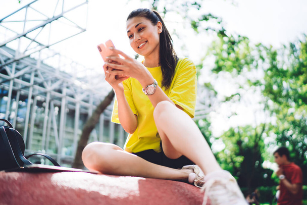 Smiling asian woman blogger in casual wear sitting on urban setting watching video on smartphone, positive hipster girl millennial typing text messages on mobile phone spending time on street - Fotografie, Obrázek