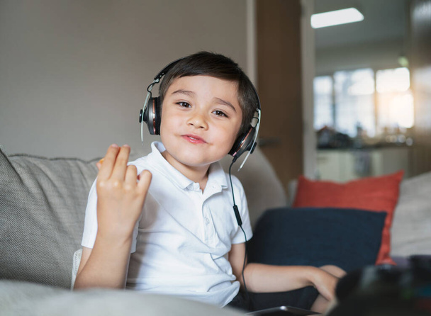 Child eating orange fruit while doing homework, Kid using tablet studying online on internet,Cute boy wearing headphone listening to music,Children with technology and social network concept - Фото, изображение