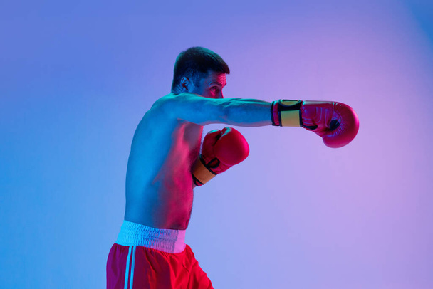 One man, professional boxer in sportwear boxing on studio background in gradient neon light. Concept of sport, activity, movement, wellbeing. - Photo, image