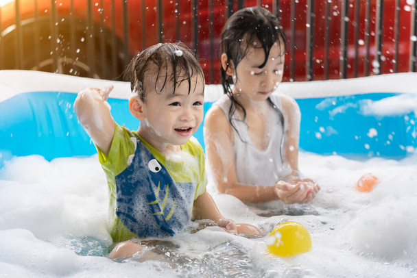 Söpö pieni poika ja sisko pitää hauskaa leikkii kuplia ja värillisiä palloja puhallettava uima-allas. Puhallettavat ja kupla-altaat, uinti kesällä, onnelliset lapset leikkivät vedessä - Valokuva, kuva