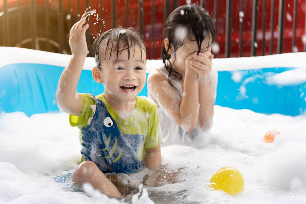 Roztomilý malý chlapec a sestra se bavit hrát s bublinami a barevné koule v nafukovací bazén. Nafukovací a bublinkové bazény, koupání v létě, veselé děti hrající si ve vodě - Fotografie, Obrázek
