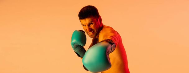 One professional male boxer in sportswear and gloves isolated on yellow studio background in neon light. Concept of sport, activity, movement. Front view - Φωτογραφία, εικόνα