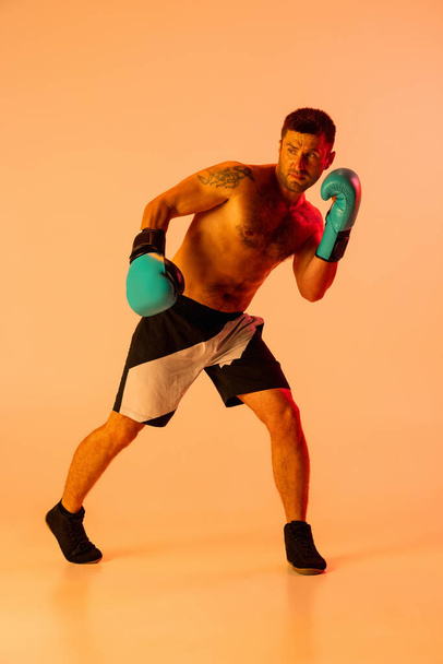 Portrait of Caucasian man, professional boxer in sportwear in action and motion on studio background in yellow neon light. Concept of sport, activity, movement, wellbeing. - Φωτογραφία, εικόνα