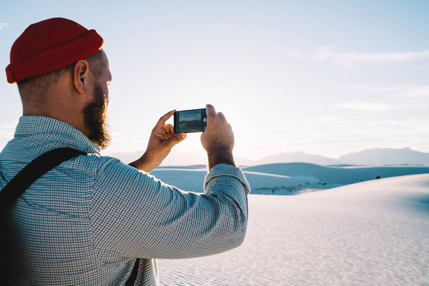 Blick zurück auf anonyme männliche Touristen in Freizeitkleidung und Hut und Rucksack, die auf Sand stehen und den White Sands National Park fotografieren - Foto, Bild
