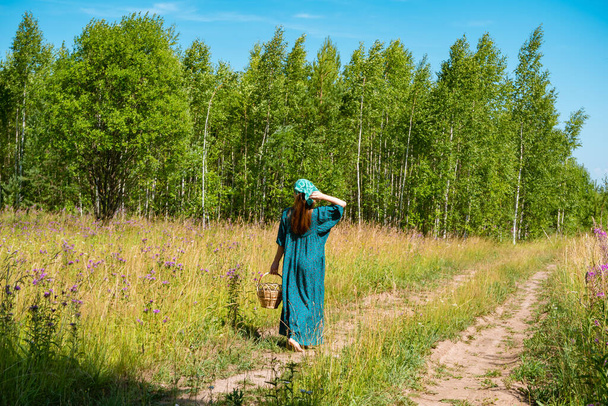 junge Frau in volkstümlicher Bauernkleidung mit Weidenkorb läuft im Sommer auf einem Feldweg - Foto, Bild