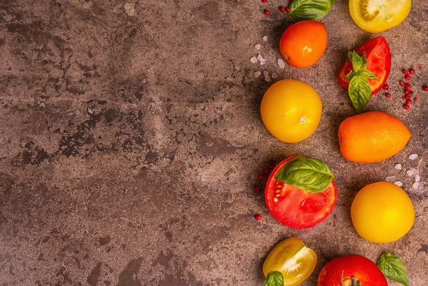 Kulinářské zázemí se zralými rajčaty a listy bazalky. Různé barevné zeleniny, mořské soli a růžové pepře na tmavém kamenném betonu pozadí, horní pohled - Fotografie, Obrázek